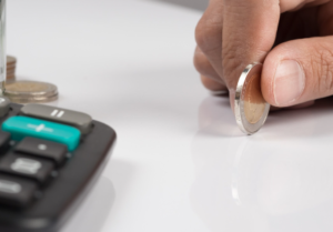 Persona colocando una moneda sobre una mesa junto a una calculadora, representando deuda en Buró de Crédito en México.