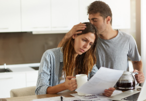 Pareja revisando una factura con preocupación en casa, representando dificultades financieras y problemas al refinanciar una deuda.